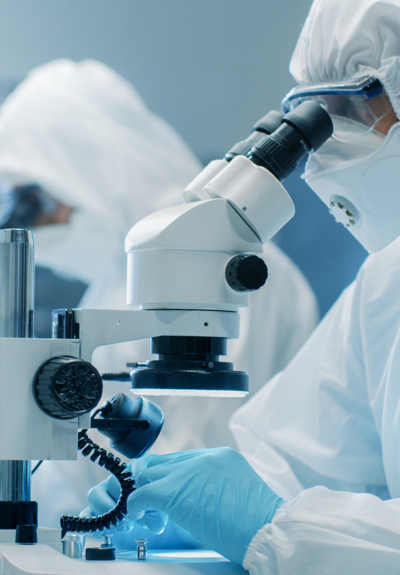 Person in white protective wear looking in a microscope